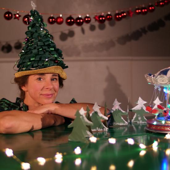 Billede af kvinde med der sidder ved bord med julepynt med en grøn hat udformet som et juletræ